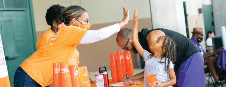 Louisiana Healthcare Connection employee high-fives a young girl at a community event, with her father in the background.